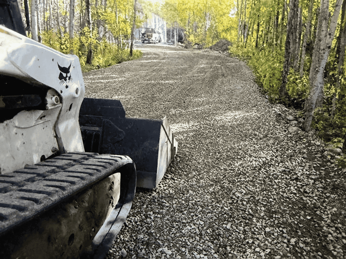 Compact track loader beside a newly installed gravel driveway through woods in Hampton Roads